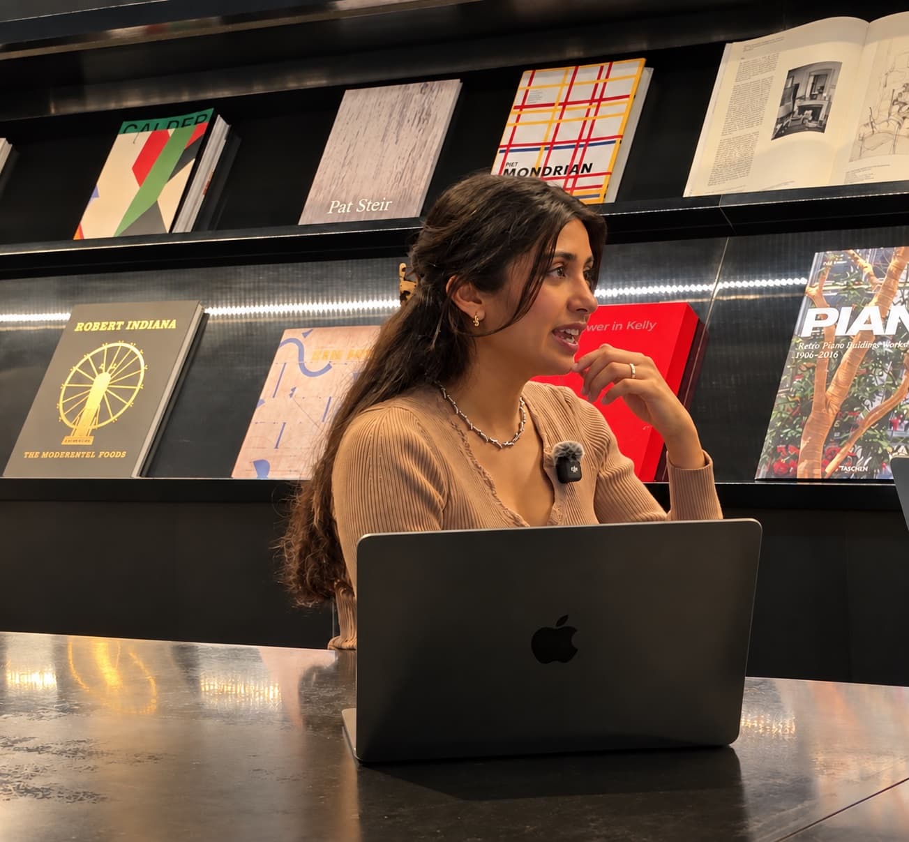 Deeya Kotecha speaking in front of bookshelves, wearing a microphone.